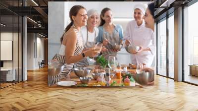 Young woman in apron drinking wine and chatting with group during master class Wall mural