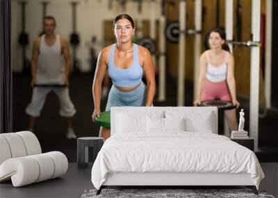 Young woman in sportswear training with weight plate in gym Wall mural