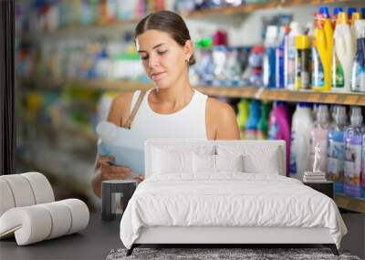 Young woman shopper choosing laundry gel in store Wall mural