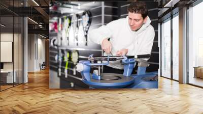 young workman is testing the tension of new tennis rocket in the store Wall mural