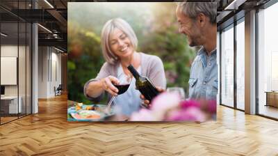  group of friends in their forties gathered around a table in the garden to share a bbq meal. A man offers red wine to a female friend Wall mural