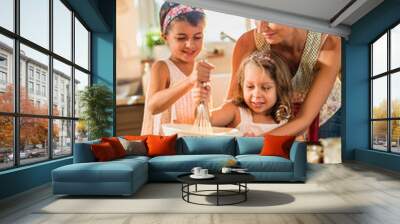 a mother is cooking a cake with her two young daughters Wall mural