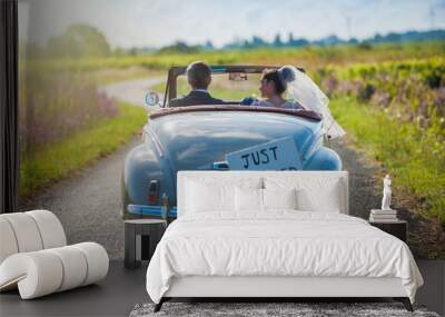 A newlywed couple is driving a retro car, rear view Wall mural