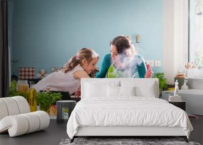 A young mother and her little daughter cooking a recipe in the kitchen Wall mural