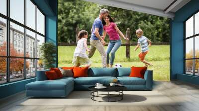 Cheerful family playing football in a garden Wall mural