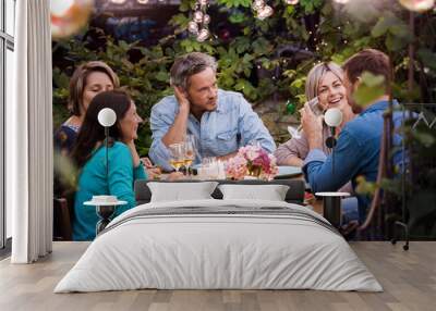 Group of  friends gathered around a table in a garden on a summer evening to share a meal and have a good time together Wall mural