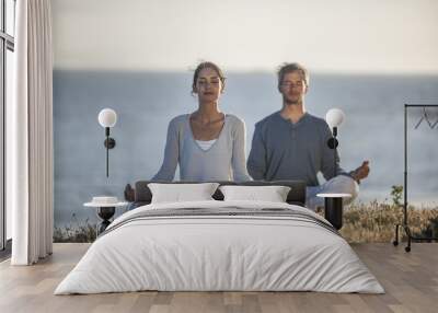 handsome couple practicing meditation exercises on the beach at Wall mural