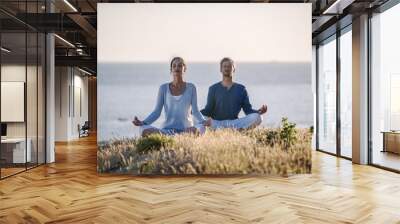 handsome couple practicing meditation exercises on the beach at Wall mural