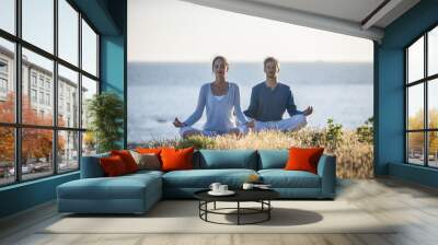 handsome couple practicing meditation exercises on the beach at Wall mural