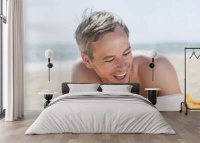 handsome man on the seaside lying on a beach towel to use a digi Wall mural