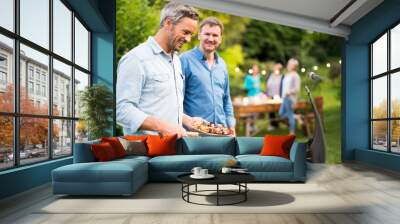 in a summer evening, two men in their forties prepares a barbecue for friends gathered around a tabl Wall mural