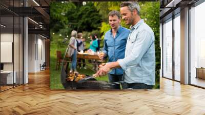 in a summer evening,  two men  in their forties prepares a barbecue for  friends gathered around a table in the garden Wall mural