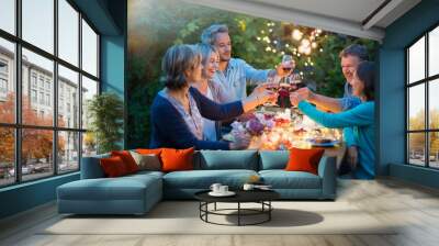 One summer evening, friends in their forties gathered around a table in the garden lit by luminous garlands. They toast with their glasses of wine Wall mural