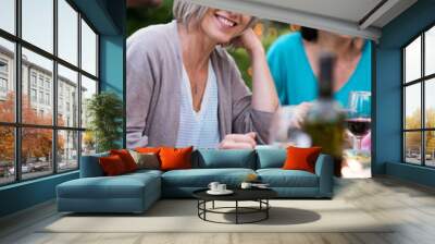 Portrait of a beautiful woman looking at camera, she sits with her friends gathered around a table in the garden one summer evening to share a meal and have fun together. Wall mural