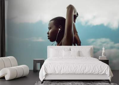 African woman with earphones doing stretching exercise Wall mural