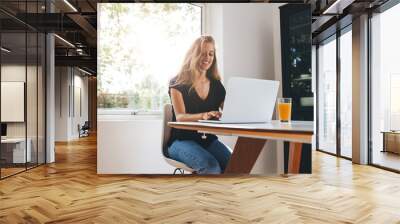 Beautiful young woman working on laptop in kitchen Wall mural