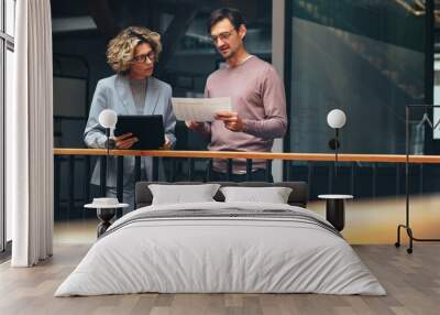 Business people reading a document together. Two professionals analyse a financial report in an office Wall mural