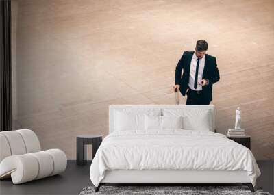 Businessman at airport terminal with suitcase and mobile phone Wall mural