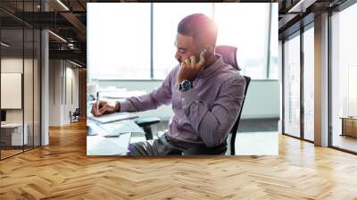 Businessman talking over mobile phone sitting at his office desk Wall mural