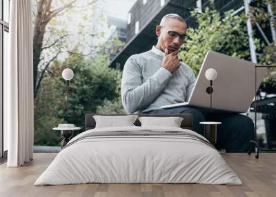 Businessman working on laptop computer sitting outdoors Wall mural