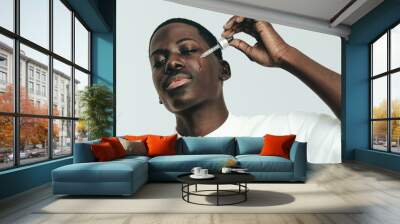 Caring for melanin skin, a young man applies beauty serum to his face Wall mural