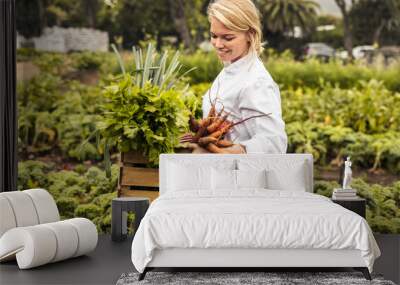 Cheerful female chef carrying fresh vegetables on a farm Wall mural