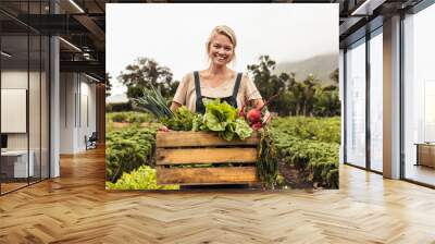 Cheerful organic farmer holding a box full of fresh produce on her farm Wall mural