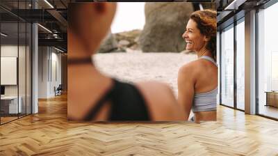 Cheerful women in fitness wear sitting on the beach Wall mural