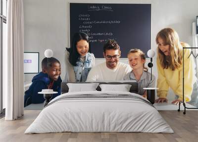 Coding school teacher showing a group of curious children how to write a code on a laptop Wall mural