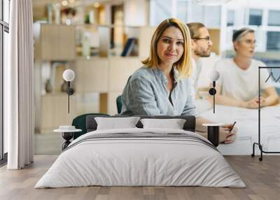 Confident young designer sitting in a meeting with her team Wall mural