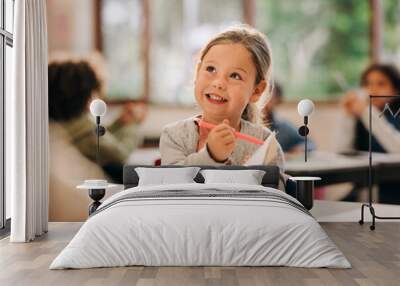 Excited little girl learns to draw with a colour pencil in an art class Wall mural