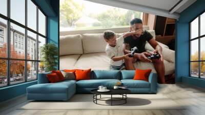 father and son having fun playing video games at home Wall mural