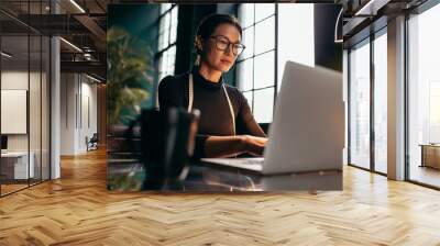 Female fashion designer working on laptop in studio Wall mural