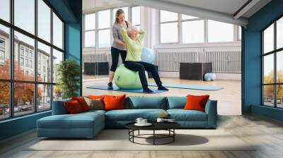 Female trainer helping senior woman exercising in gym Wall mural