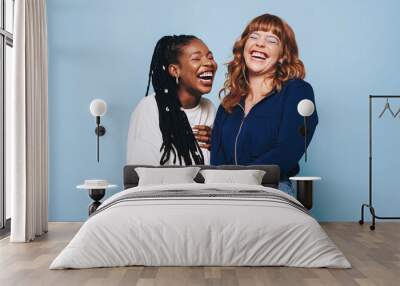 Funny best friends laughing cheerfully while standing together in a studio Wall mural