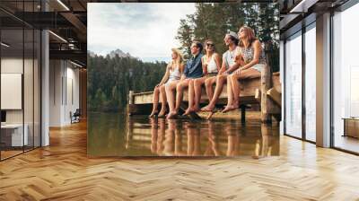 Group of friends sitting on jetty at lake Wall mural