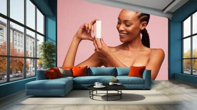 Happy african woman holding a cosmetic product Wall mural