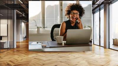 Laughing businesswoman sitting at her work desk Wall mural