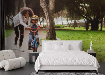 Little boy learning to ride bicycle at park with mother Wall mural