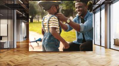 Man helping son wearing helmet for cycling at park Wall mural