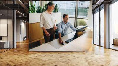 Manager standing by employee working in office Wall mural