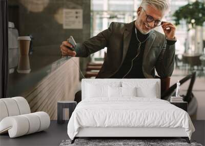 Mature businessman at cafe listening music from cellphone Wall mural