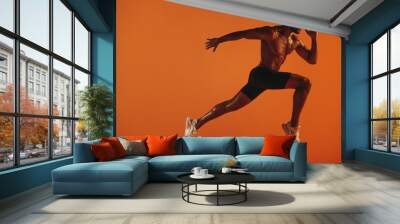 Muscular athlete running on orange background Wall mural