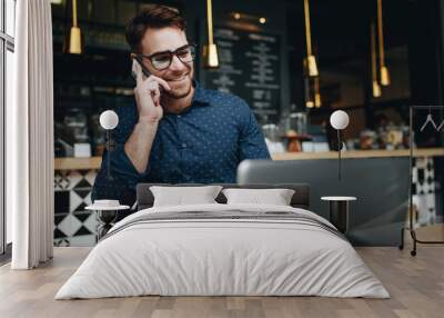 Smiling businessman talking on cell phone while working on lapto Wall mural