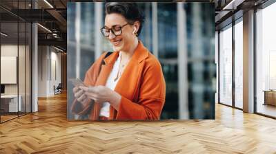 Smiling businesswoman reading a text message on her phone while commuting to her office in the city Wall mural