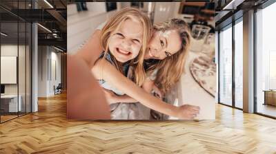 Smiling little girl and woman in kitchen taking selfie Wall mural