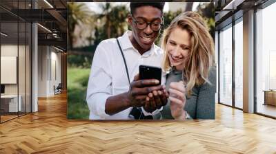 Smiling multiracial couple looking at pictures on phone Wall mural