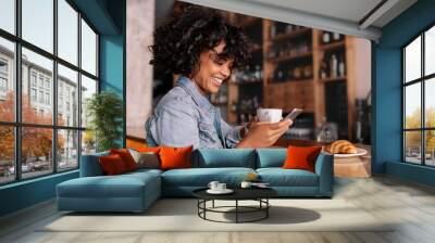 Smiling woman using smart phone in a modern cafe Wall mural