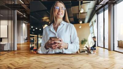 Thoughtful businesswoman holding a smartphone Wall mural