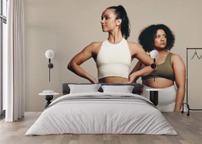 Two fit young women stand together in sportswear, embracing a healthy lifestyle in the studio Wall mural